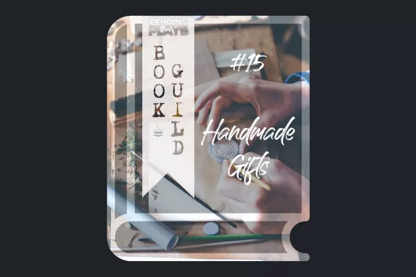 A book icon with a photo that shows an art desk with art utensils and the hands of a human who's crafting a sigil/stamp for a letter. Photo by Annie Spratt from Unsplash. A bookmark on the left side of the book, with the Pending Plays logo at the top and "Book Guild" in vertical format below. On the right of the book it says "#15 Handmade Gifts" in a bold font with dripping liquid.