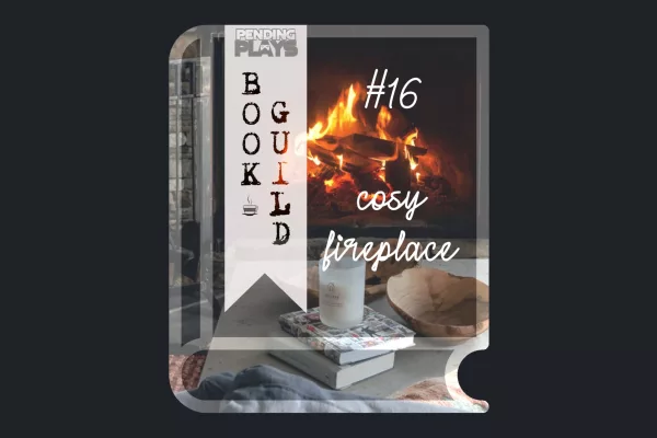 A book icon with a photo that shows a fire burning in a stone fireplace in a living room. In Front is a table with two books, a candle, wooden bowls, and blankets. Photo by Clay Banks from Unsplash. A bookmark on the left side of the book, with the Pending Plays logo at the top and "Book Guild" in vertical format below. On the right of the book it says "#16 cosy fireplace" in a cursive, handwritten font.
